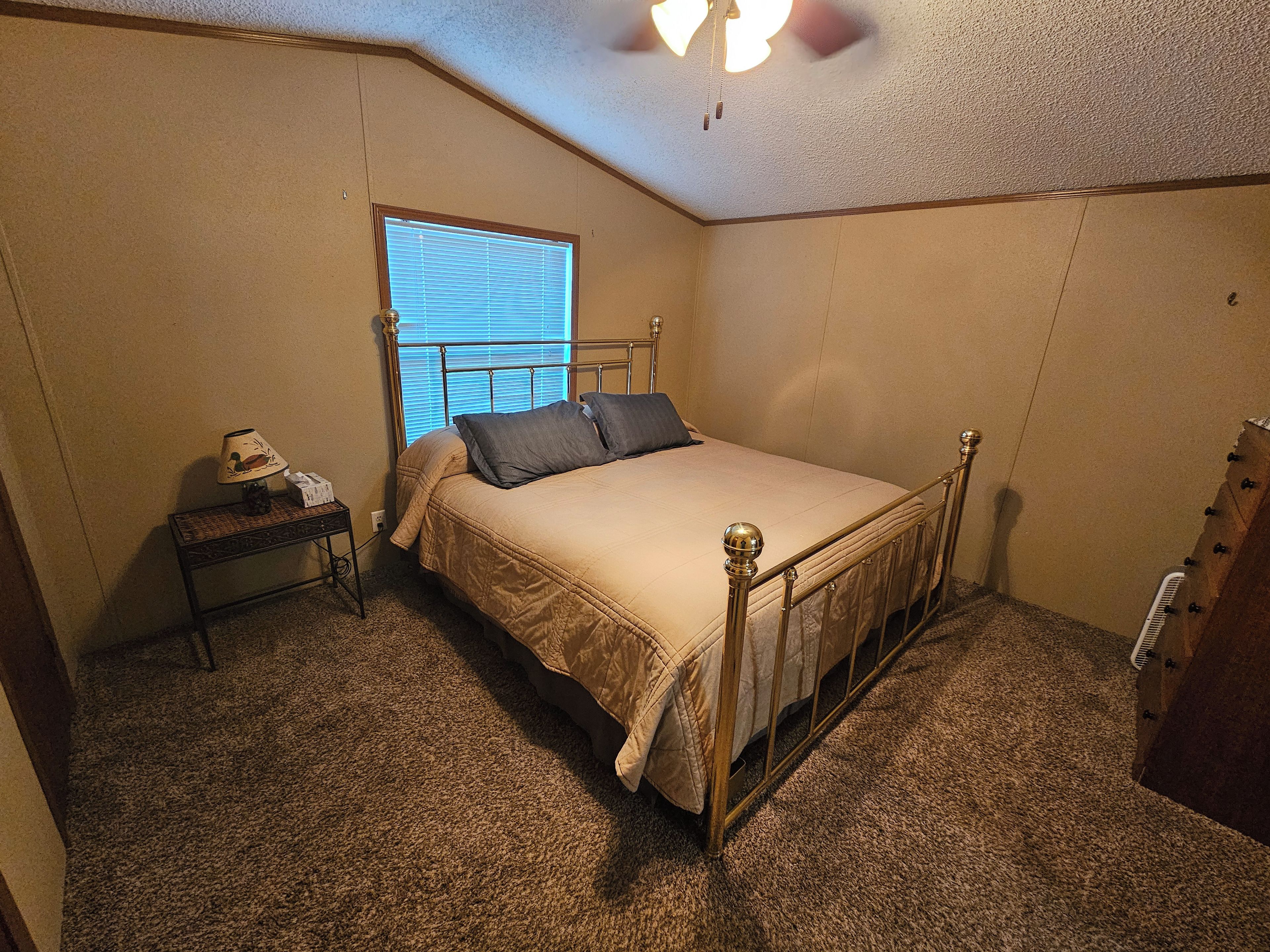 A bedroom with a single bed, a bedside table, a lamp, and a window with blinds.