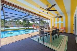 Un espacio al aire libre techado con piscina, sillas y una mesa.