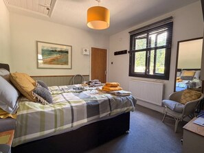Ein Schlafzimmer mit einem Bett, einem Sessel, einem Fenster mit Jalousien, einem Heizkörper und einem Bild an der Wand.