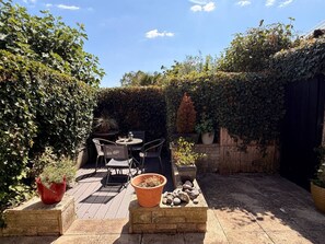 Ein Patio mit Tisch und Stühlen, umgeben von Blumentöpfen und einem Holzzaun.