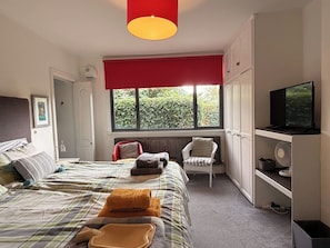 Een slaapkamer met een bed, een stoel, een televisie en een raam.