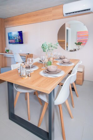 Un comedor con una mesa de madera dispuesta para cuatro personas, sillas blancas y una cocina moderna al fondo.