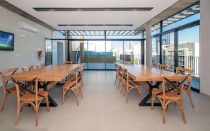 Uma sala de conferências com uma longa mesa de madeira e cadeiras, amplas janelas com vista para a cidade e um extintor de incêndio na parede.