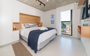 Quarto moderno com cama, mesas de cabeceira, obras de arte, televisão e vista para uma varanda.