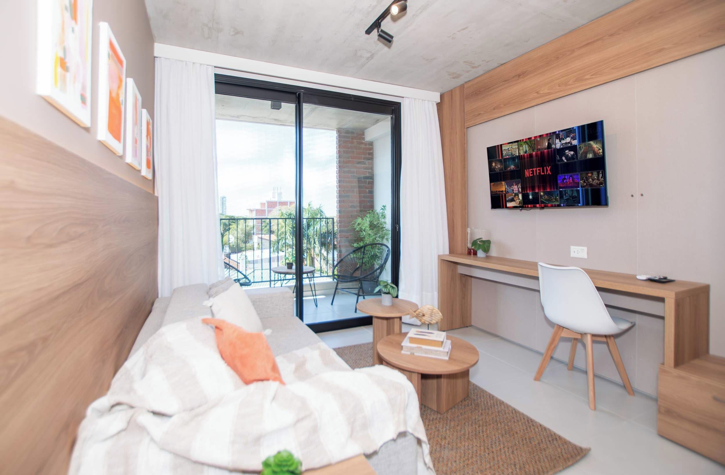 Una sala de estar moderna con un sofá, una mesa de centro, un escritorio con una silla y una amplia pantalla de televisión mostrando contenido de Netflix.