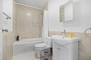 A bathroom with a bathtub, toilet, sink, and a shower curtain. - Cozy Toronto 3BR Escape | Spacious Family Friendly (Toronto)