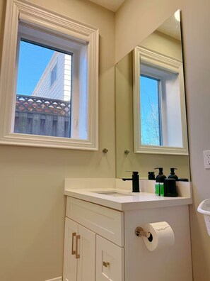 Een badkamer met een raam, wastafel, spiegel en toilet.