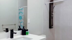 Uma casa de banho moderna com um lavatório branco, um espelho grande, um chuveiro com mangueira preta e uma sanita branca.
