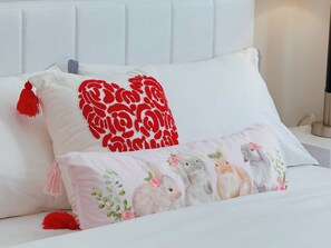 Een bed met twee kussens, één met een rood bloemenmotief en het andere met een konijnenprint.
