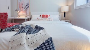 Quarto de hotel com uma cama grande, mesa de cabeceira com abajur, uma cadeira e um quadro na parede.