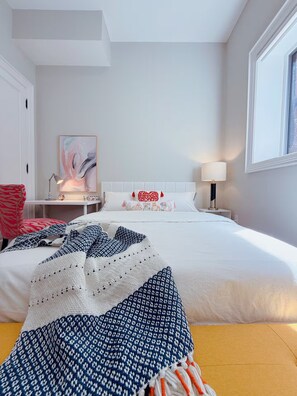 Een hotelkamer met een groot bed, een nachtkastje met een lamp, een stoel en een schilderij aan de muur.