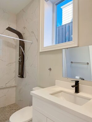Ein Badezimmer mit Dusche, Toilette und Waschbecken mit Spiegel darüber.