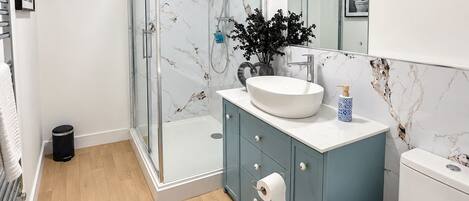 Un baño moderno con ducha envuelta en vidrio, un lavamanos blanco y un inodoro.