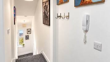 A hallway with a grey carpet, a white wall, and two framed paintings of rabbits. There are hooks on the wall and a white telephone.