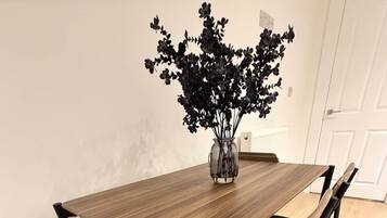A dining table with a vase of flowers, four chairs, and a white door in the background.