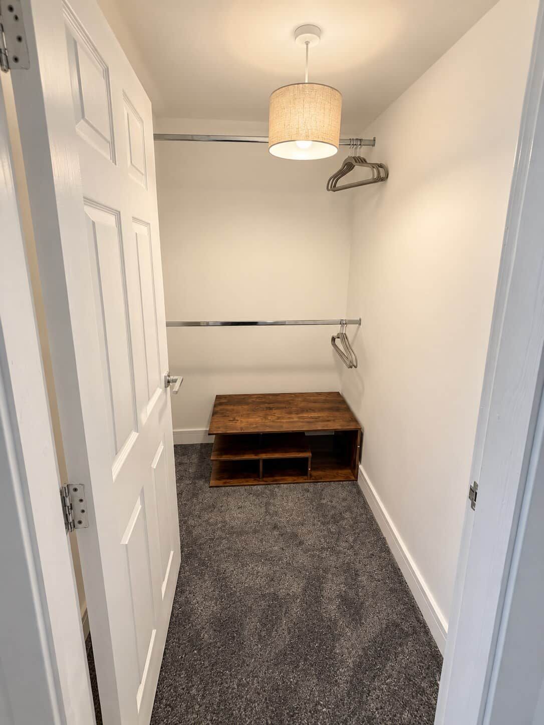 A narrow hallway with a wooden bench, a white door, and a hanging light fixture.