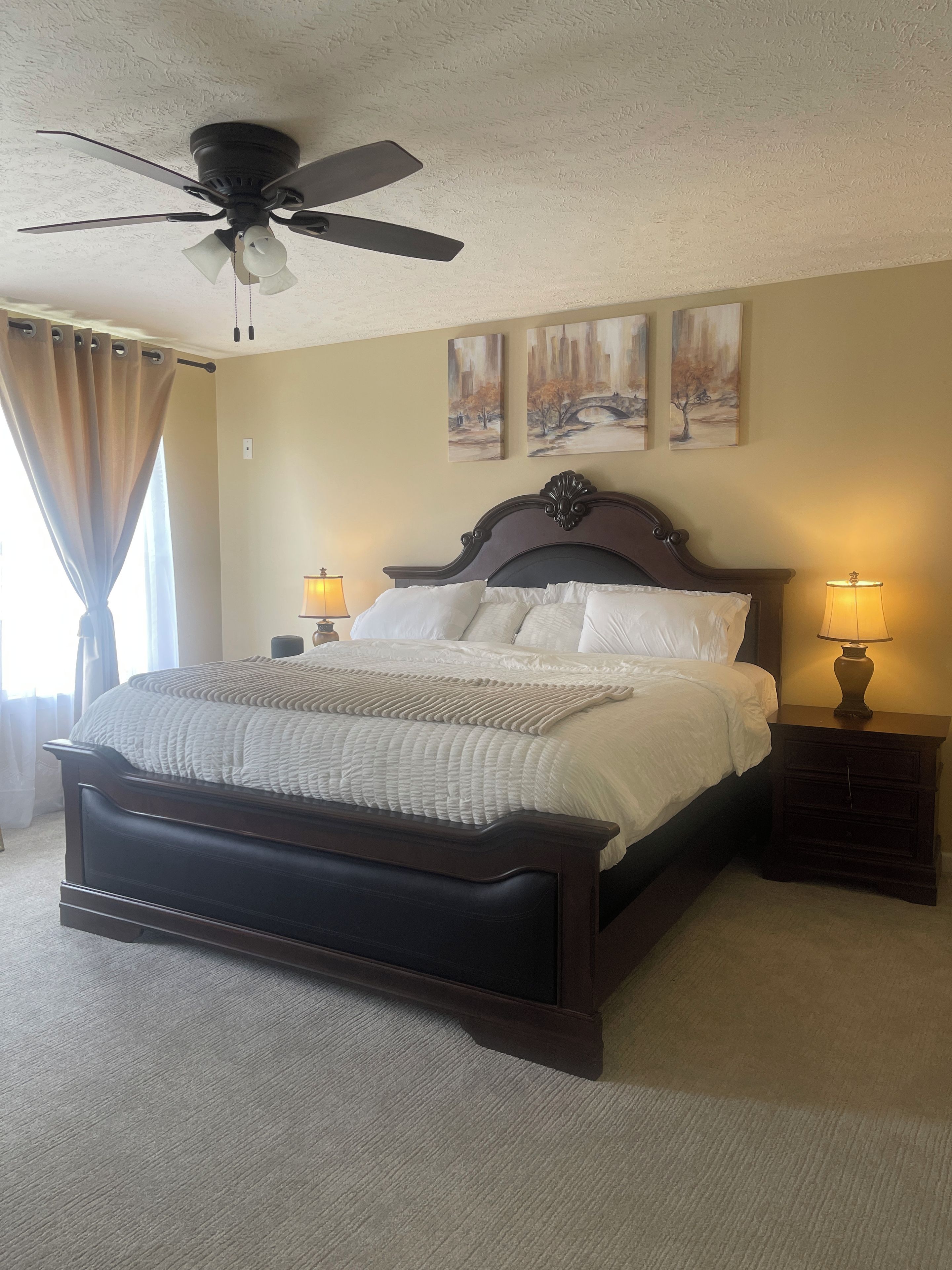 A bedroom with a bed, two bedside lamps, a ceiling fan, and artwork on the wall.