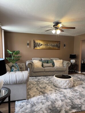 A living room with a ceiling fan, a sofa, a coffee table, a fluffy rug, and a painting on the wall. - Spacious 4BR Home Sleeps 8, 3Baths Family-Friendly & Comfortable 🏡 (Akron)