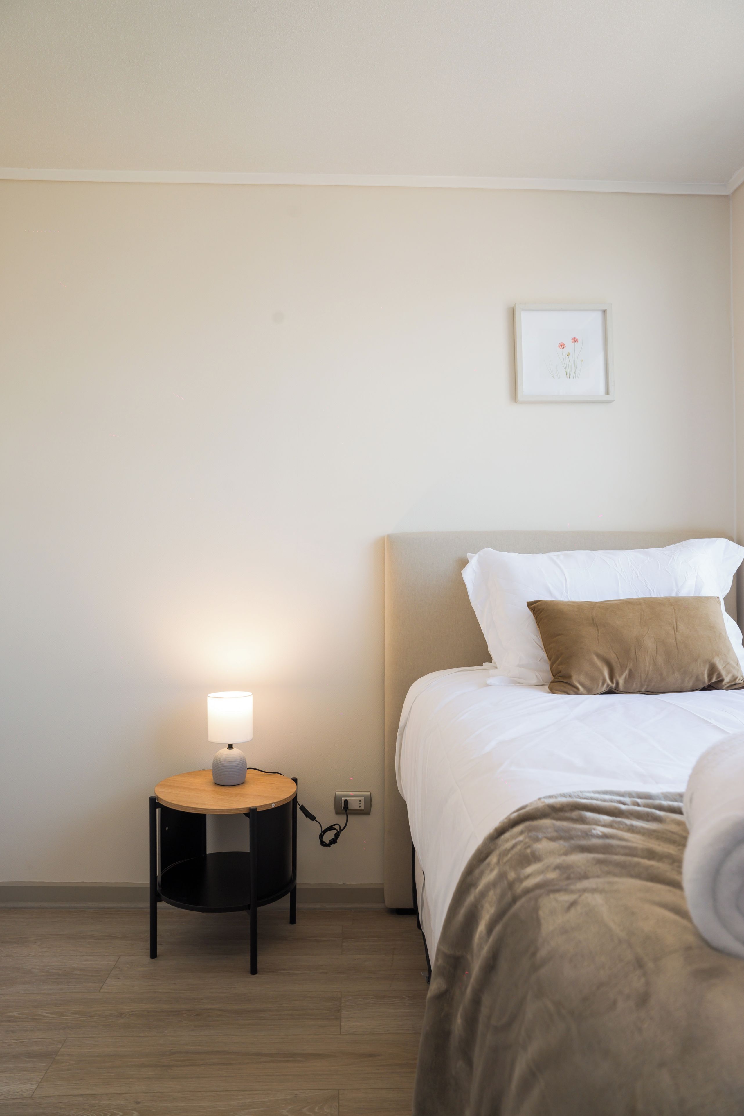 A bedroom with a bed, a bedside table with a lamp, and a wall-mounted picture.