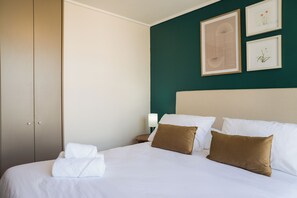 Een hotelkamer met een bed, kussens, een nachtkastje, een lamp en kunst aan de muur.