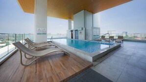 Área de piscina no terraço com espreguiçadeiras, piscina e vista para a cidade.