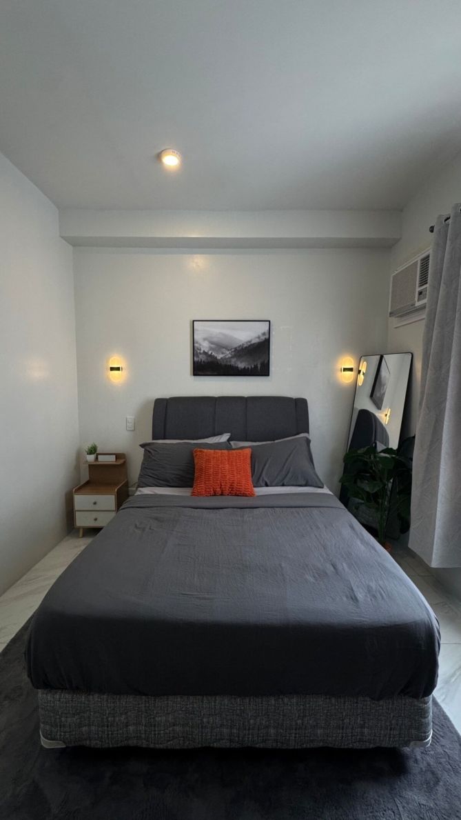 A modern bedroom with a large bed, bedside tables, a wall-mounted light, and a framed picture.