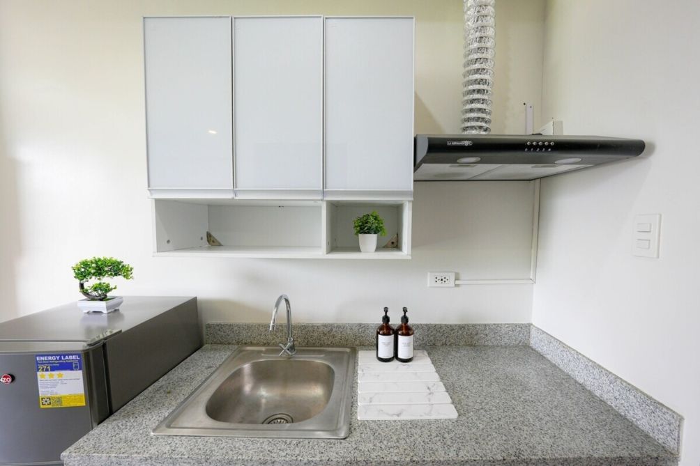 Een keuken met een roestvrijstalen spoelbak, witte kasten, een kleine plant in een pot en twee flessen op het aanrecht.