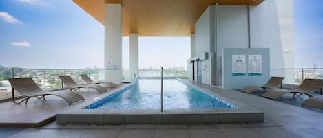 Una piscina en la azotea con sillones de descanso y vistas a la ciudad.