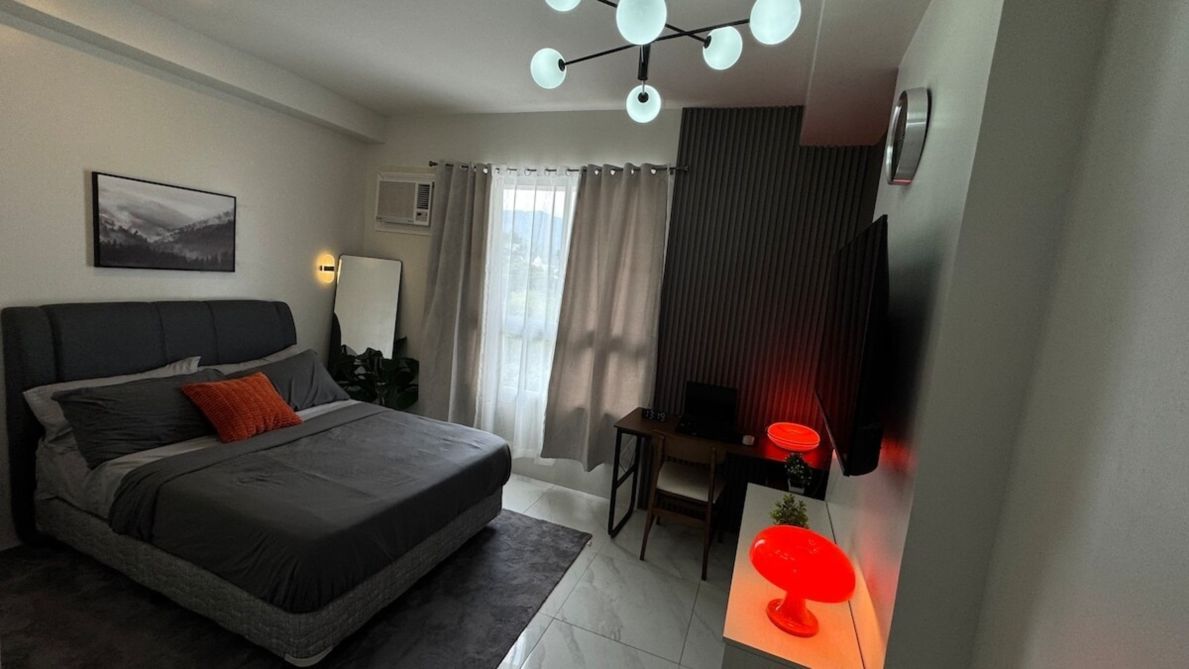 Ein modernes Schlafzimmer mit einem Bett, einem Schreibtisch, einem Stuhl, einem Fernseher und einem Fenster mit Vorhängen.