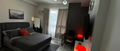 A modern bedroom with a bed, a desk, a chair, a TV, and a window with curtains.