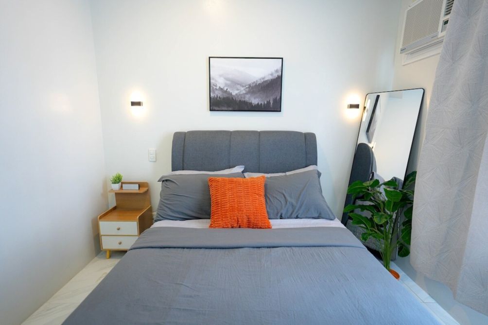 A bedroom with a bed, bedside table, nightstand, and a mirror.