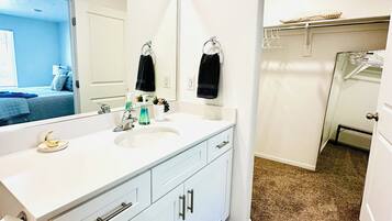 Une salle de bain avec un meuble-lavabo blanc, deux vasques, un miroir et un porte-serviettes.
