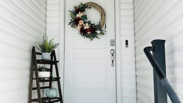A white door with a wreath, a wooden ladder with plants, and a black welcome mat.