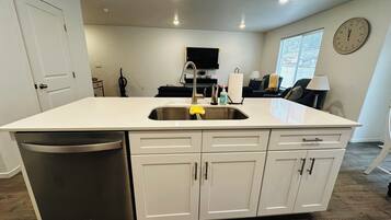 A modern kitchen with a stainless steel sink, white cabinetry, and a built-in dishwasher.