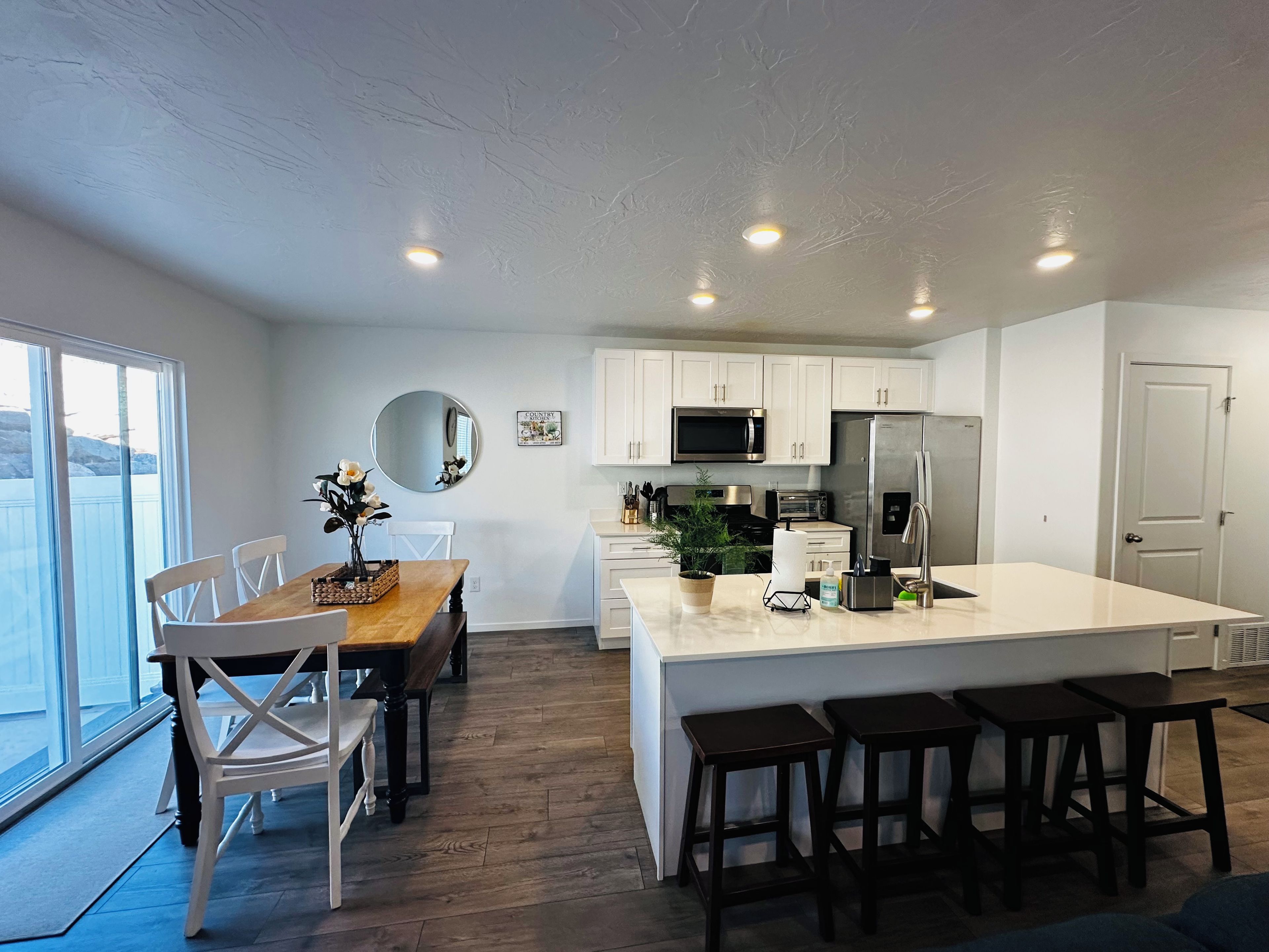 Une cuisine moderne avec des meubles blancs, un îlot central et un coin repas comprenant une table et des chaises en bois.
