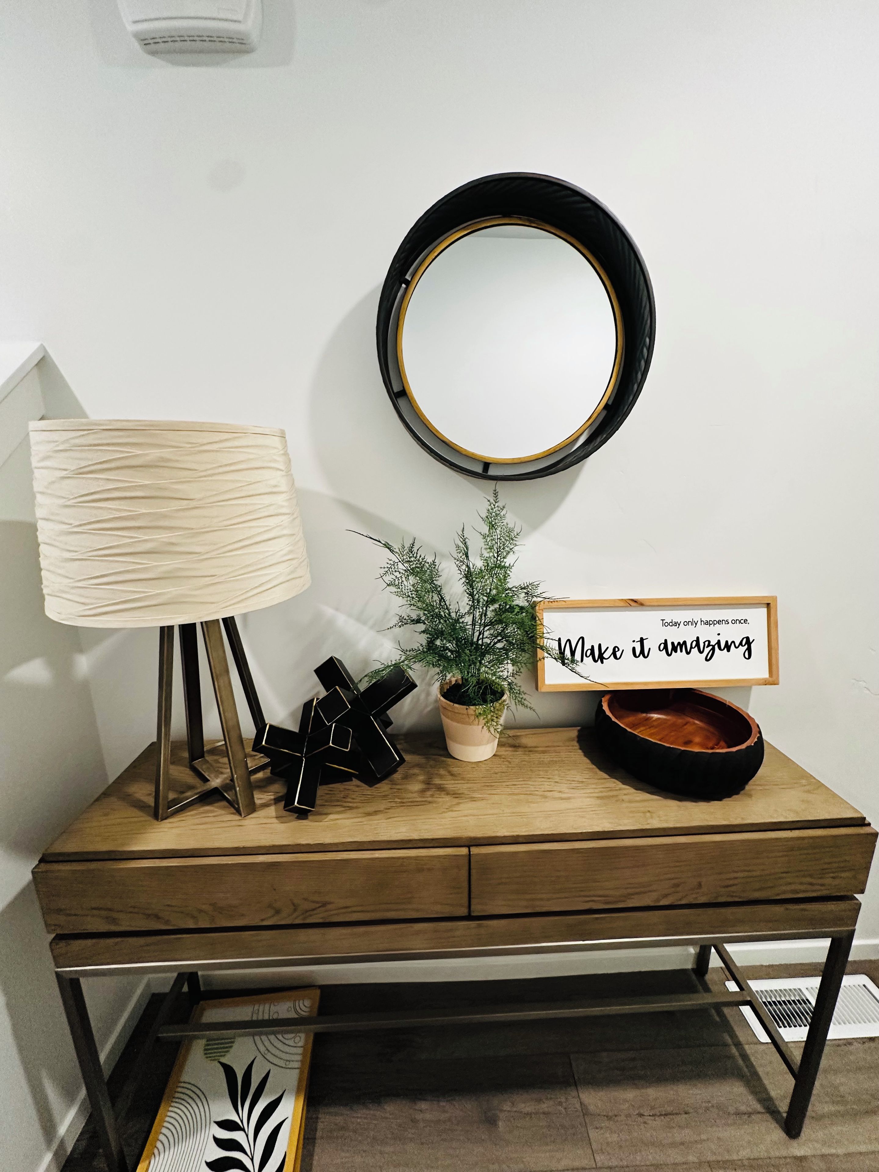 A wooden desk with a lamp, a potted plant, a mirror, and a motivational sign.