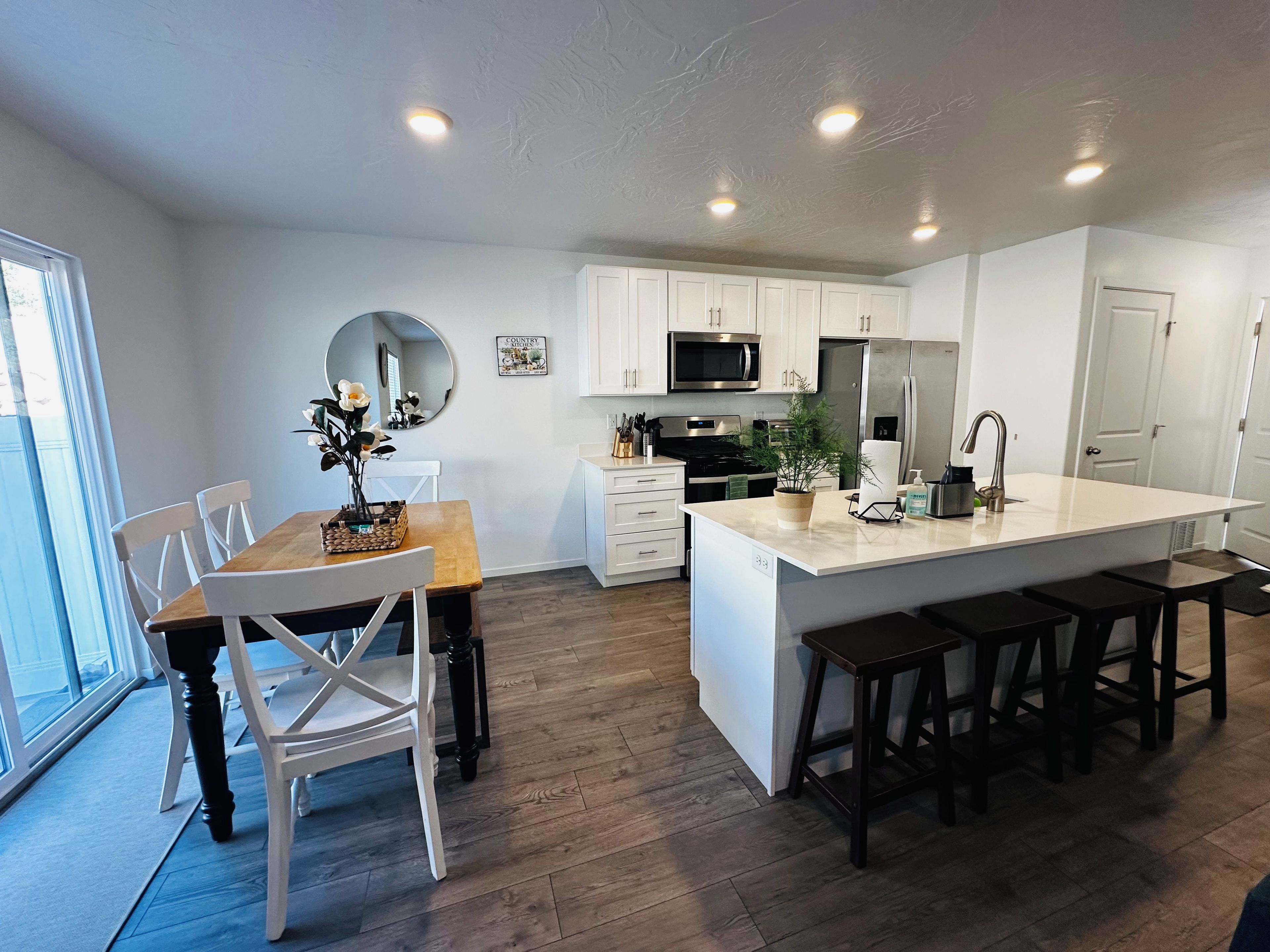 A modern kitchen with white cabinetry, a central island, and a dining area with chairs.