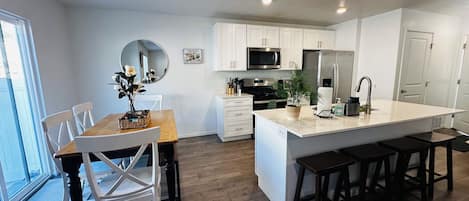 A modern kitchen with white cabinetry, a central island, and a dining area with chairs.