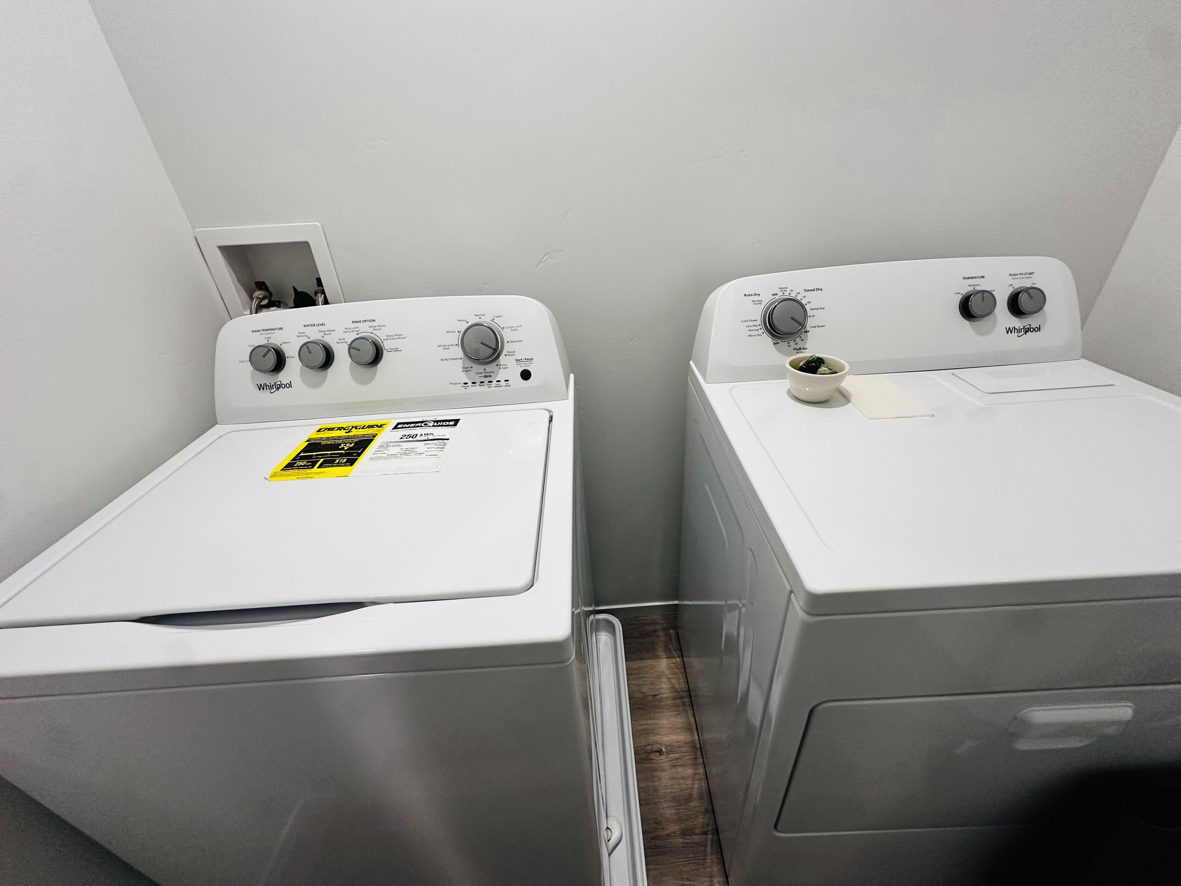 Two white Whirlpool washers in a laundry room with a visible water inlet and outlet.