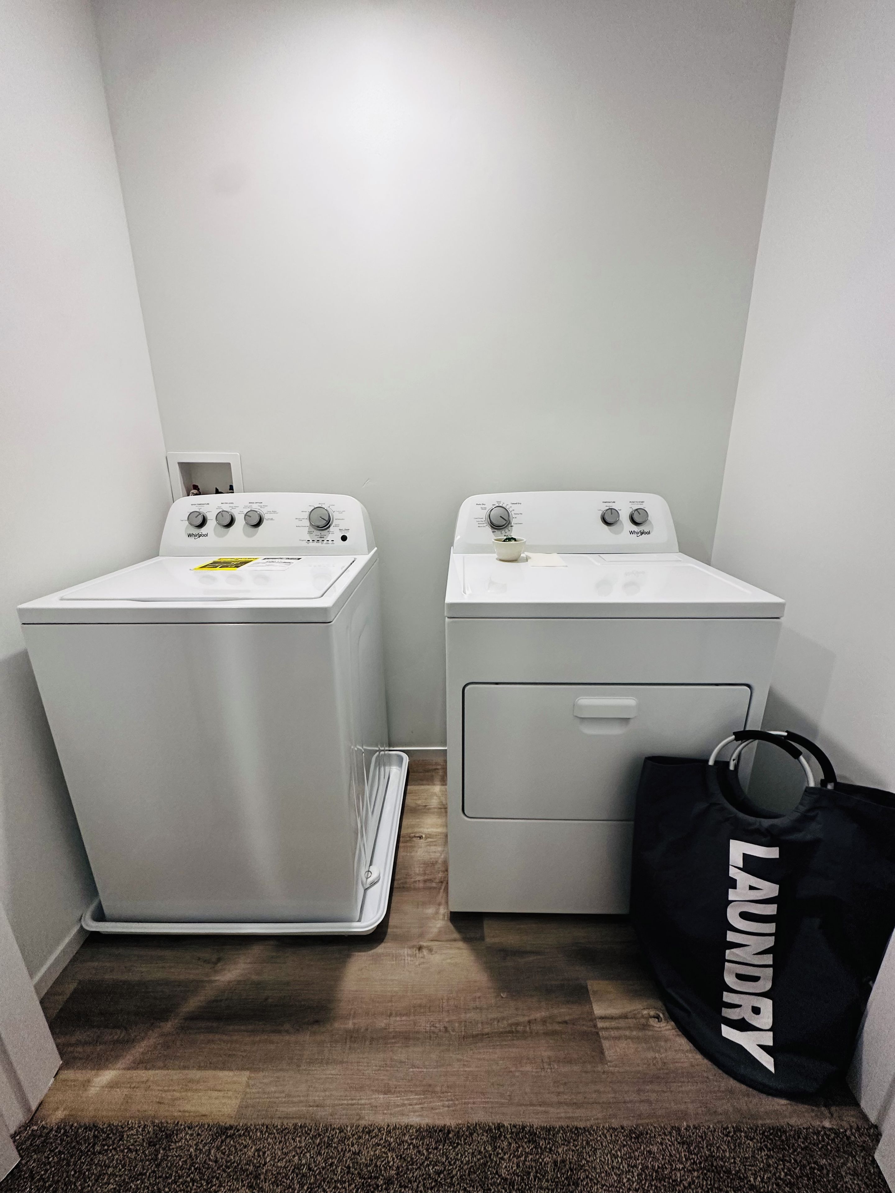 A laundry room with two front-loading washing machines and a black laundry bag.