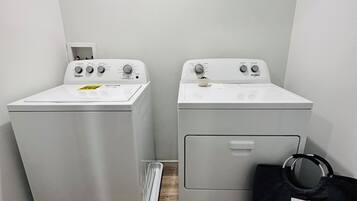 A laundry room with two front-loading washing machines and a black laundry bag.