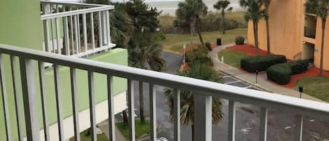 A balcony with a view of the ocean and a building with a palm tree garden.