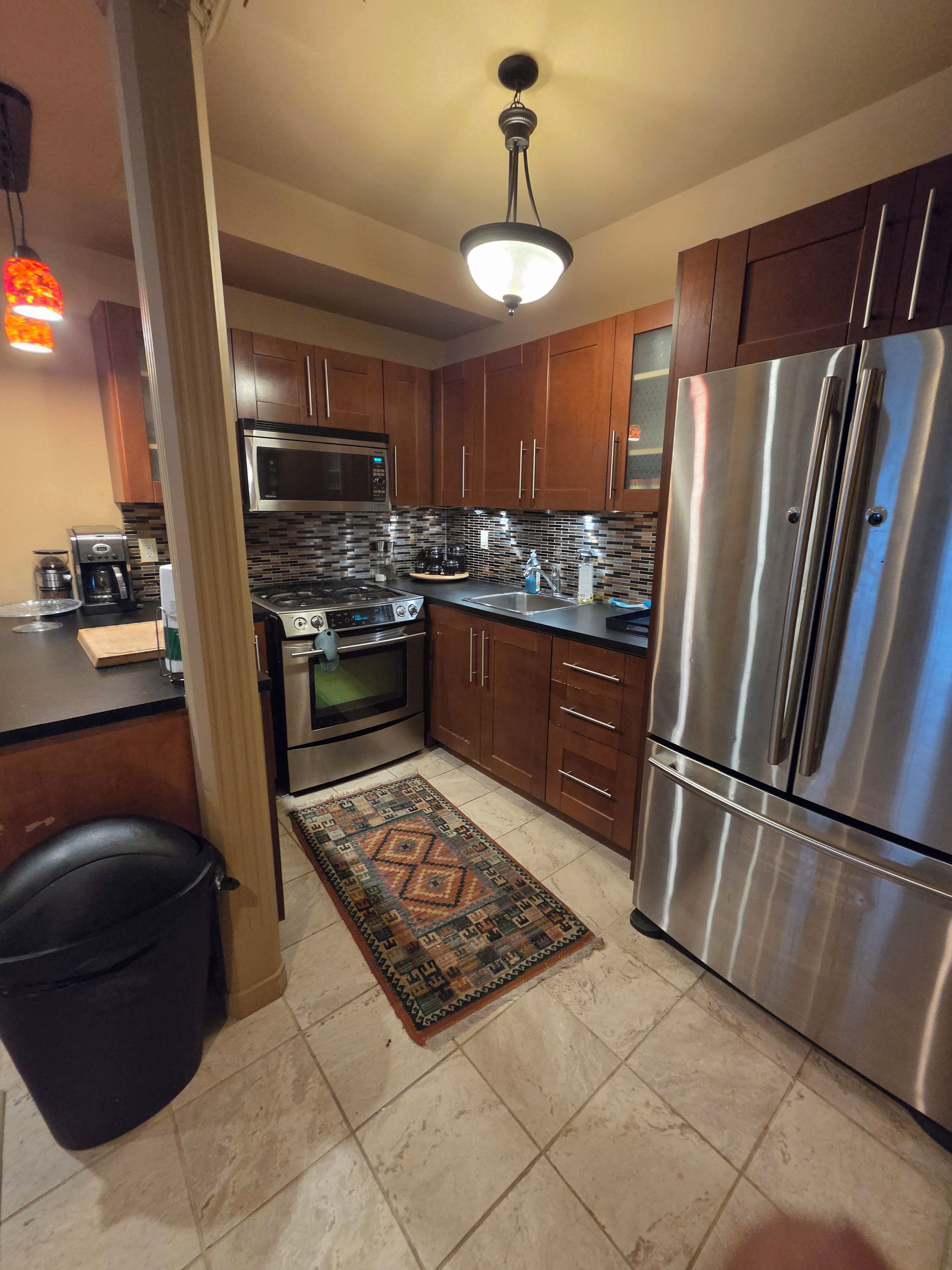 A modern kitchen with stainless steel appliances, wooden cabinets, and a patterned rug.