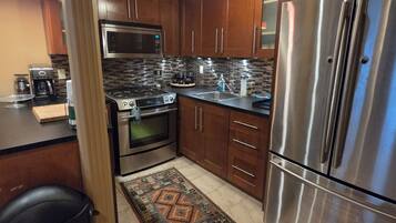 A modern kitchen with stainless steel appliances, wooden cabinets, and a patterned rug.
