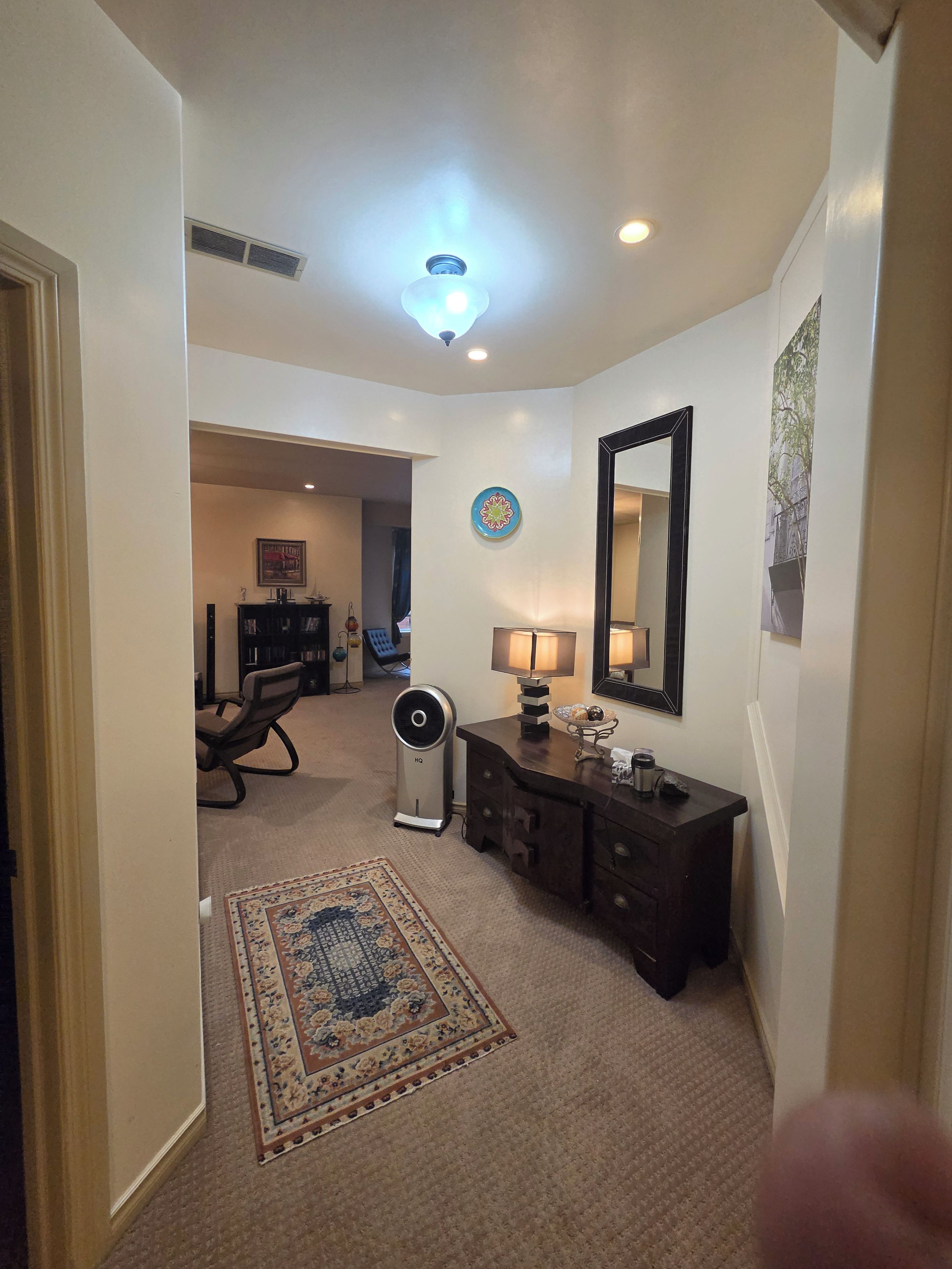 A hallway with a ceiling fan, a rug, a dresser, and a mirror.