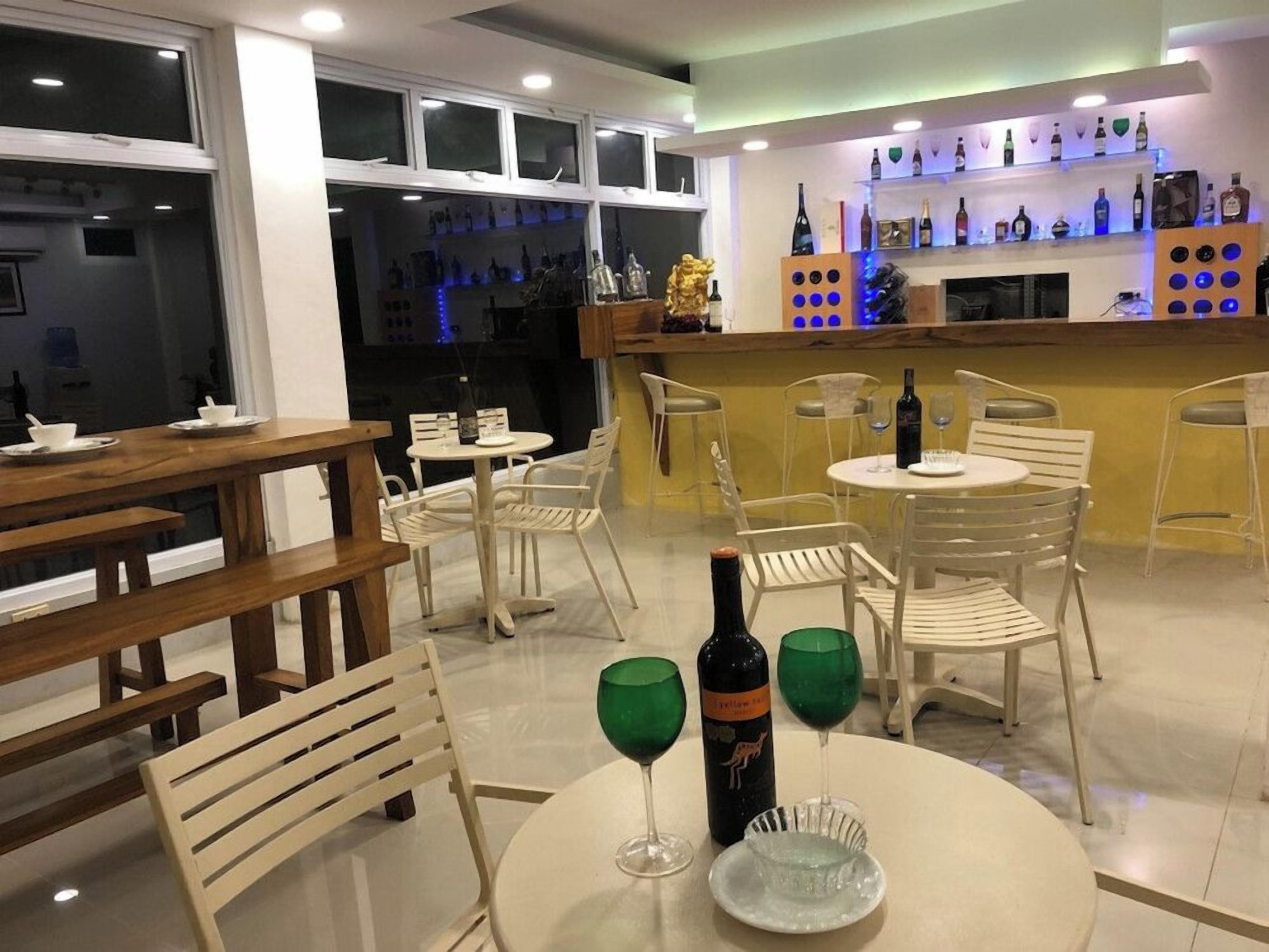 Un restaurant avec des tables et des chaises rondes, un bar avec des étagères remplies de bouteilles, et une bouteille de vin posée sur une table.
