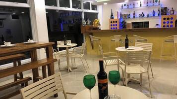 Un restaurant avec des tables et des chaises rondes, un bar avec des étagères remplies de bouteilles, et une bouteille de vin posée sur une table.