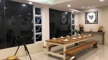 Un coin repas avec une longue table en bois, dressée pour quatre personnes, des bancs de chaque côté et un trépied en arrière-plan.