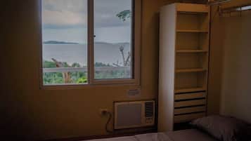 A room with a large window overlooking a body of water, a bed, and a built-in shelving unit.