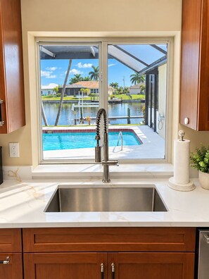 A kitchen with a view of a swimming pool and a window with a view of a residential area. - 3-bedroom house in gorgeous Cape Coral with pool and deck (Cape Coral)